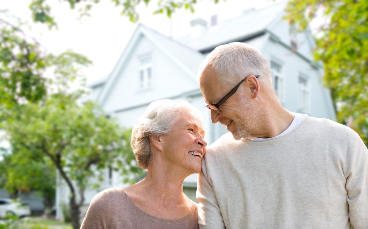 family, age, home, real estate and people concept - happy senior couple hugging over living house background